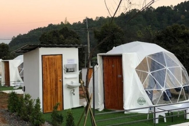 Geodesic domes with wooden doors and outdoor washstations in a wooded area at sunset.