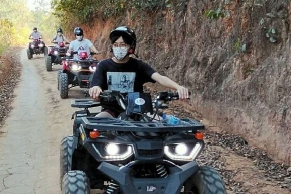People riding ATVs on a narrow, tree-lined dirt path.