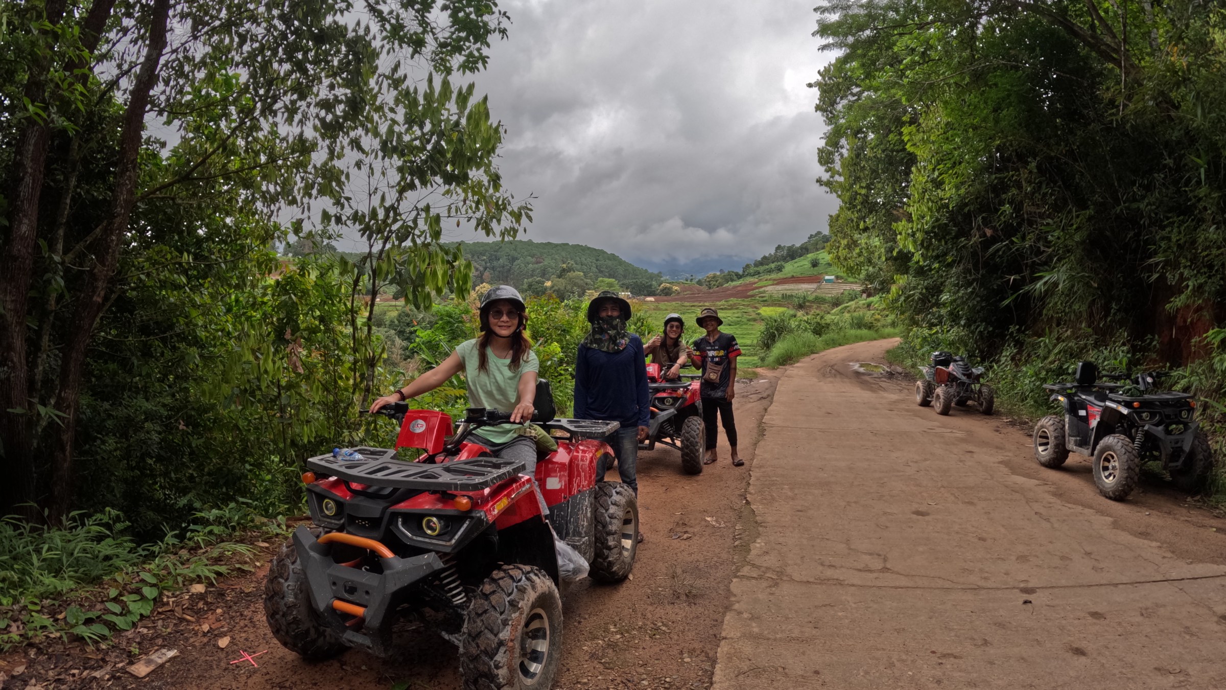 People riding ATVs on a forest trail under cloudy skies.