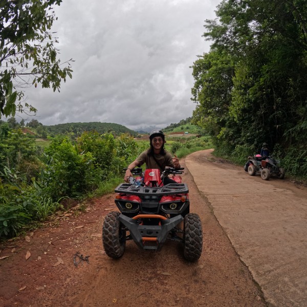 Person on a quad bike on a rural path bordered by lush greenery.