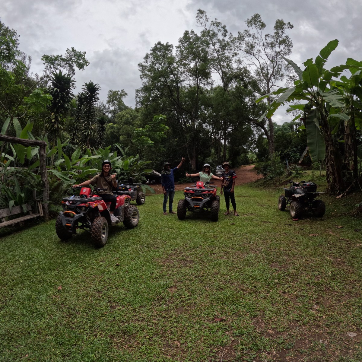 People on ATVs in a lush, tropical setting with trees and greenery.
