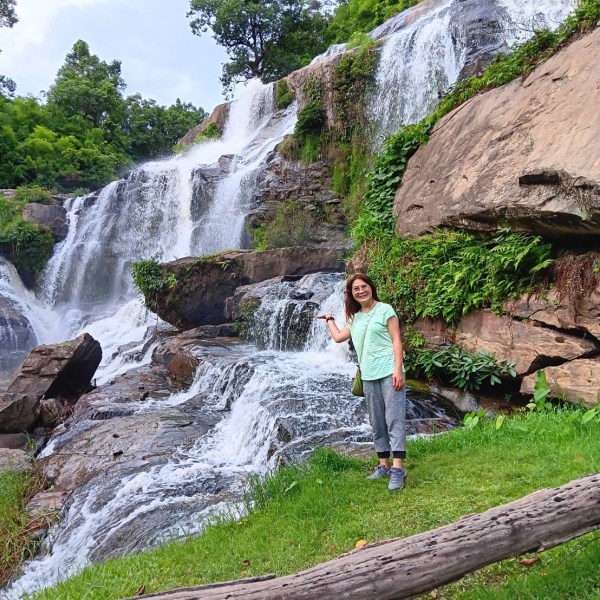 Woman posing by a multi-tiered waterfall with greenery.
