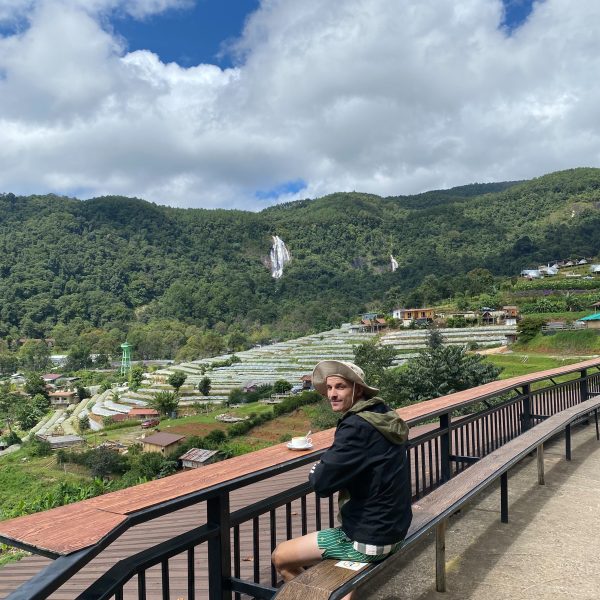 Person sitting on bench with scenic mountain view and cloudy sky.