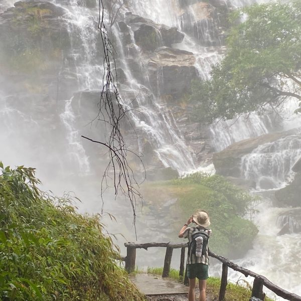 Person standing on path, photographing large waterfall.
